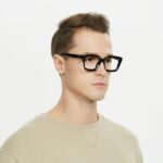 Portrait of a young man wearing black glasses, showcasing modern fashion in a studio setting.